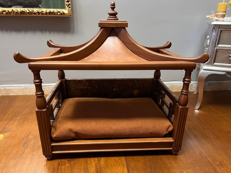 May include: A wooden dog bed with a pagoda-style roof. The bed has a brown cushion and is made of dark wood.
