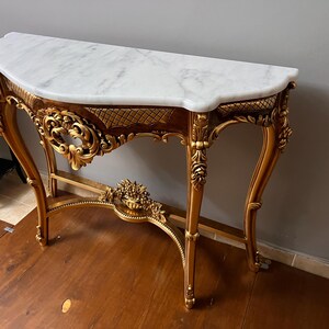 May include: A gold-painted console table with ornate carvings and a white marble top.