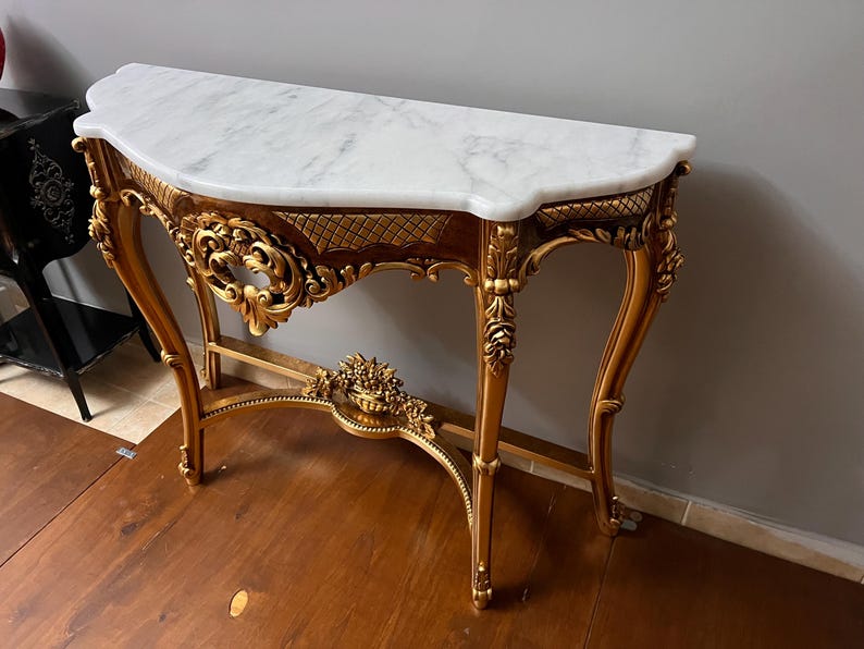 May include: A gold-painted console table with ornate carvings and a white marble top.