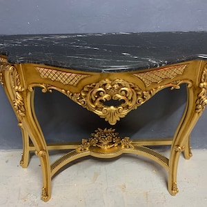 May include: A gold-painted console table with intricate carvings and a black marble top.