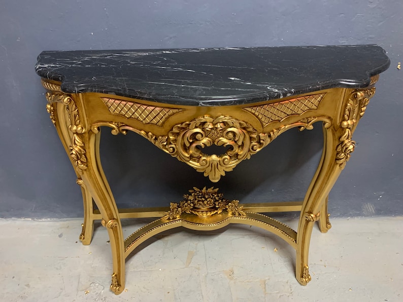 May include: A gold-painted console table with intricate carvings and a black marble top.