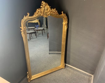 May include: A large, ornate gold-painted mirror with a decorative, carved frame. The mirror is rectangular and has a beveled edge.