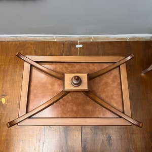 May include: A wooden coffee table with a brown leather top and a decorative wooden base. The table has a rectangular shape and is supported by four curved legs.
