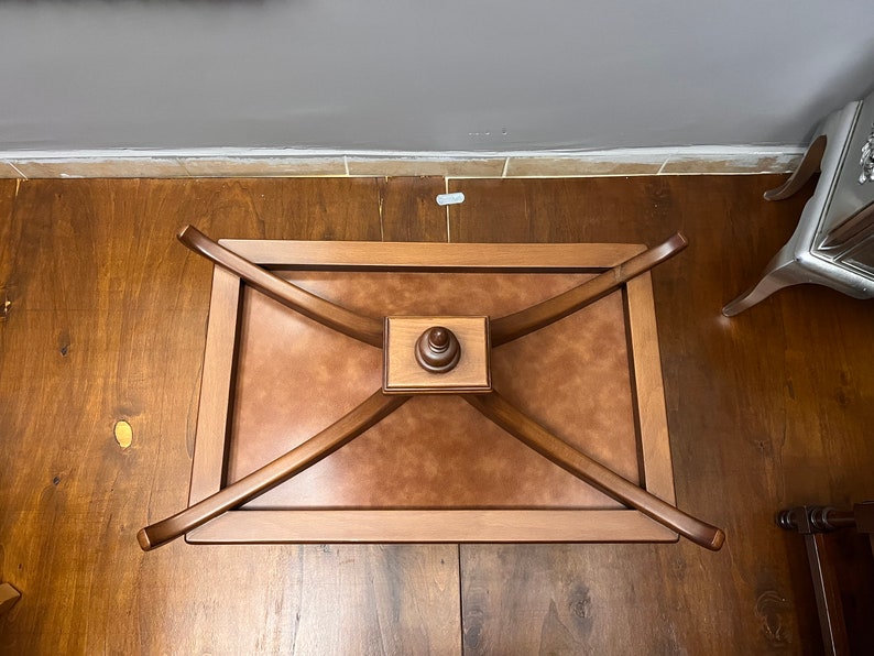 May include: A wooden coffee table with a brown leather top and a decorative wooden base. The table has a rectangular shape and is supported by four curved legs.