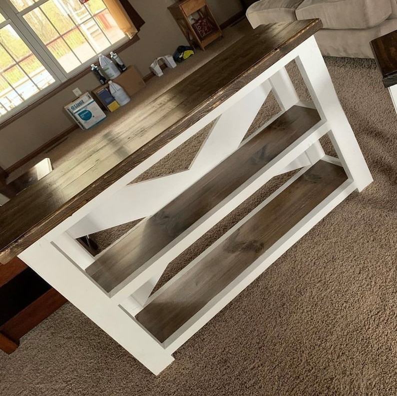 May include: A white and brown wooden console table with two shelves. The table has a farmhouse style with a white painted frame and a brown stained top and shelves.