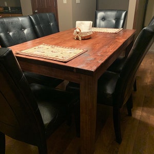 May include: A dark wood dining table with a natural finish. The table has a rectangular top and four legs. Six black leather chairs surround the table.