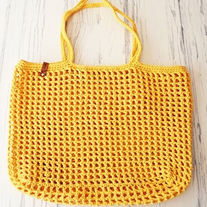 May include: A yellow crocheted tote bag with leather handles. The bag has a square grid pattern.