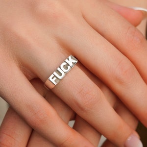 May include: A silver ring with the word "FUCK" spelled out in raised letters.