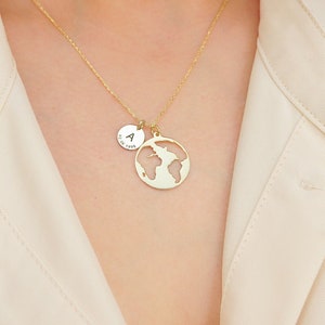 May include: A gold necklace with a small round charm and a larger charm shaped like the world. The smaller charm has the letter "A" engraved on it.