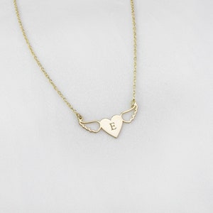 Op de afbeelding: Een gouden ketting met een hartvormige hanger met een enkele letter 'E' en vleugels.