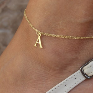 May include: A gold chain anklet with a letter 'A' charm.