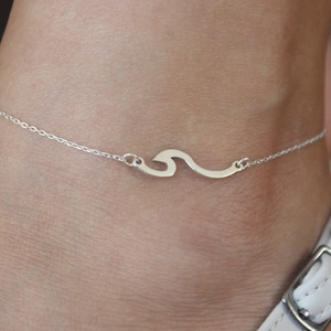 May include: A silver ankle bracelet with a wave charm. The bracelet is delicate and has a simple design.