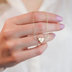Op de afbeelding: Een gouden ketting met een hartvormige hanger met een enkele initiaal "E" en kleine vleugels aan beide kanten.