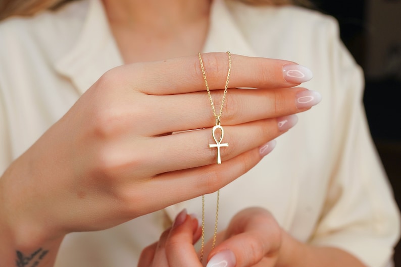 K&ouml;nnte beinhalten: Eine goldene Kettenkette mit einem Ankh-Anh&auml;nger. Der Ankh ist ein Symbol des Lebens in der alten &auml;gyptischen Mythologie.
