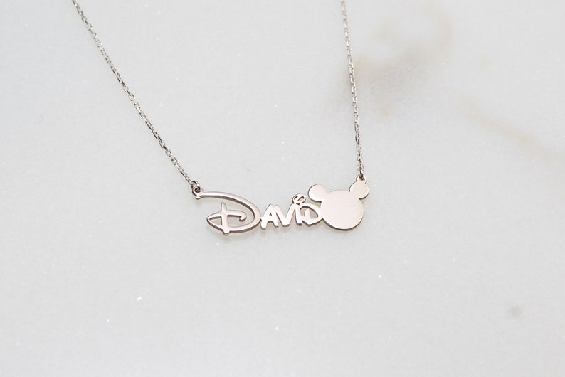 Puede incluir: Collar de plata con una cabeza de Mickey Mouse y el nombre "David" en una fuente de Disney.