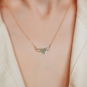 Op de afbeelding: Een gouden ketting met een hartvormige hanger met delicate vleugels. Het hart is glad en de vleugels zijn gedetailleerd.