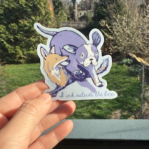 May include: A sticker featuring a cartoon illustration of a fox and a dog in shades of purple, tan, and white. The sticker has the text "I ink outside the box."