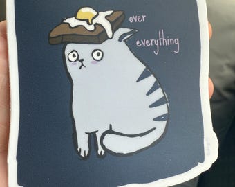 Over Everything Egged Cat sticker / vinyl decal. Featuring a cat with toast and a fried egg on her head. She just can not.