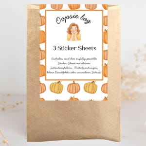 Könnte beinhalten: Ein brauner Papiersack mit einem weißen Etikett mit der Aufschrift "Oopsie bag" und "3 Sticker Sheets". Das Etikett hat ein Kürbismuster und eine Zeichnung einer Person. Der Beutel enthält Stickerbögen mit kleinen Fehlern.