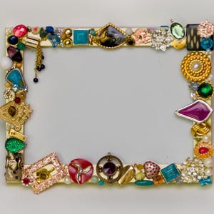May include: A gold picture frame decorated with colorful jewels, rhinestones, and beads. The frame is made of wood and has a white background.