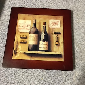 May include: A framed print featuring two wine bottles, corks, and a corkscrew. The bottles have labels, and the print has a rustic, vintage aesthetic. The frame is a dark brown color.