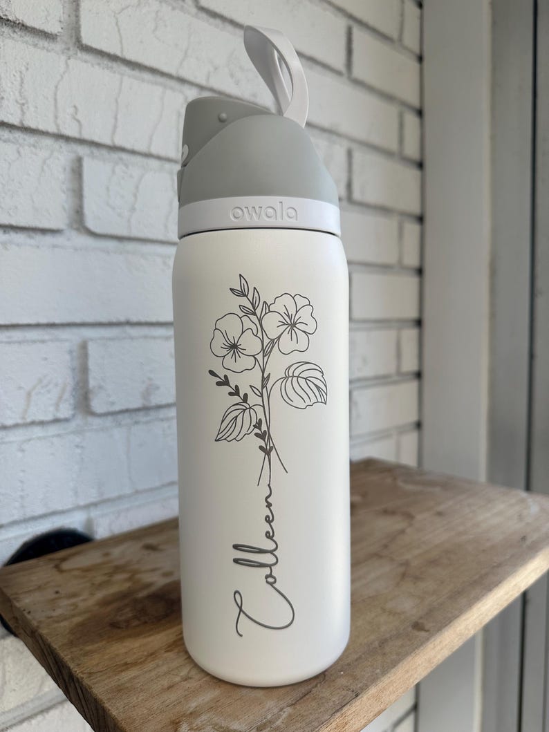 Puede incluir: Una botella de agua blanca con tapa y asa grises. La botella presenta un dise&ntilde;o floral y el nombre "Colleen" en cursiva. La marca "awala" est&aacute; impresa en la tapa.