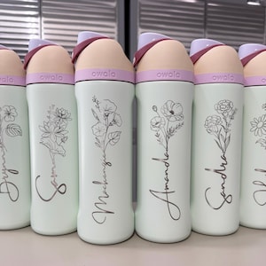 Puede incluir: Seis botellas de agua Owala en fila, cada una con un nombre diferente en escritura cursiva y un dise&ntilde;o floral. Las botellas son de color verde claro con una tapa rosa y beige. Los nombres son Brynne, Sophie, Mackenzie, Amanda, Sandra y Hailey.