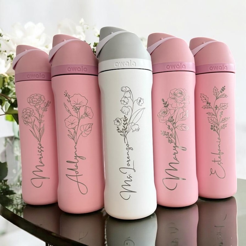 Puede incluir: Una colecci&oacute;n de botellas de agua aisladas en rosa y blanco. Cada botella presenta un dise&ntilde;o floral y un nombre. La botella blanca tiene una tapa gris, mientras que las botellas rosas tienen tapas rosas. La marca "awala" est&aacute; impresa en las tapas.