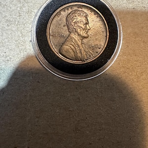 May include: A copper-colored 1914 Lincoln penny coin in a plastic coin holder with a black rim.