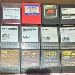 May include: A collection of Atari video game cartridges, including titles like "Chicken," "Claim Jumper," "Millipede," and "Asteroids." The cartridges are in various colors and feature game titles and Atari branding.