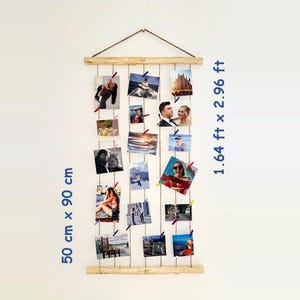 Op de afbeelding: Een houten fotodisplay met meerdere foto's bevestigd met kleine clips. Het display is 50 cm x 90 cm. De foto's zijn van verschillende formaten en tonen mensen en landschappen.