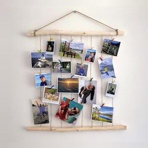 Peut inclure: Un présentoir photo en bois avec plusieurs photos accrochées à de la ficelle. Le présentoir est fait de bois naturel et de ficelle, avec une corde de suspension en haut. Les photos sont de tailles variées et présentent différentes scènes et personnes, maintenues par des pinces colorées.