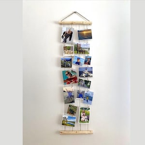 Könnte beinhalten: Ein Holz-Bilderrahmen mit einem Seil und Clips zum Aufhängen von Fotos. Der Rahmen enthält 14 Fotos von verschiedenen Landschaften und Personen.