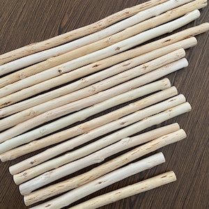 Pu&ograve; includere: Una collezione di tasselli di legno di colore chiaro, disposti diagonalmente su una superficie di legno marrone scuro. I tasselli hanno un aspetto naturale, non rifinito, con nodi visibili e variazioni di colore.
