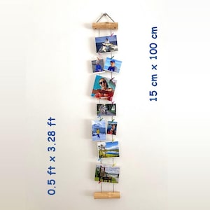 Op de afbeelding: Een verticale fotodisplay van hout en metaal, met een afmeting van 15 cm x 100 cm. Het bevat meerdere foto's die met kleine clips zijn bevestigd. De foto's tonen mensen en landschappen. Het hout is van natuurlijke kleur.