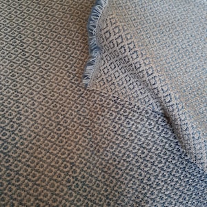 May include: A close-up of a fabric with a geometric pattern. The fabric is a gradient of blue and white, with a subtle sheen. The fabric is woven with a fine texture.