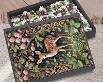 May include: A jigsaw puzzle box with a detailed illustration of a fawn lying in a forest setting with pink flowers and green foliage. The box is open, revealing the puzzle pieces. The box is dark gray.