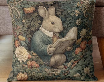 May include: Decorative square pillow featuring a rabbit in a blue jacket reading a book. The rabbit is surrounded by flowers and foliage in shades of green, orange, and cream. The pillow has a vintage, storybook aesthetic.