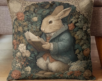 May include: Decorative square pillow featuring a rabbit in a blue coat reading a book amidst a floral and foliage background. The pillow has a vintage aesthetic with a detailed illustration and a soft color palette of greens, browns, and creams. The pillow is designed for home decor.