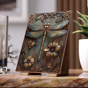 May include: A decorative wooden plaque featuring a detailed relief of a dragonfly and flowers. The dragonfly has blue and gold wings, with a gold body. The flowers are brown and gold, set against a teal background. The plaque is displayed on a wooden stand.