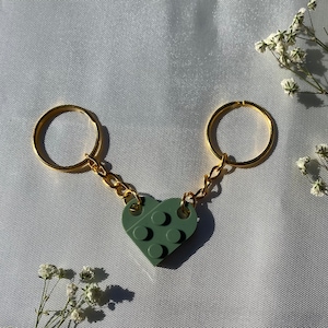 Könnte beinhalten: Ein grüner herzförmiger Schlüsselanhänger aus Lego-Steinen, befestigt an zwei goldenen Schlüsselringen mit einer goldenen Kette.