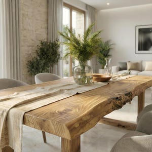 May include: A solid wood dining table with a live edge. The table is rectangular and has a light brown finish. A beige table runner and a clear glass vase with green plants are on the table. Two grey chairs are in front of the table.