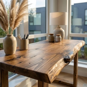 May include: A solid wood desk with a natural edge, showcasing a warm brown finish. The desk is paired with a beige lamp, decorative jars, and a vase with dried pampas grass. The desk measures approximately 152 cm long.