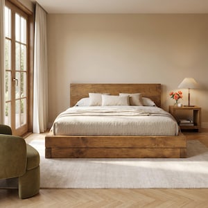 May include: A wooden bed frame and headboard in a bedroom setting. The bed is constructed from light brown wood and features a low platform. It is made up with a beige duvet and pillows. A small wooden bedside table holds a lamp and flowers.