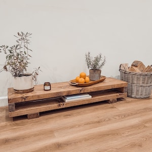 Può includere: Un mobile TV rustico in legno con un ripiano inferiore. Il mobile è tinto di un marrone caldo e ha una forma rettangolare. È decorato con piante, arance, una candela e un cesto di legna da ardere. Il mobile misura 152 cm di lunghezza.