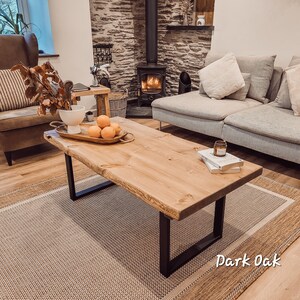 May include: A rustic wooden coffee table with black metal legs. The table has a natural wood finish and is made of reclaimed wood. The table is sitting on a rug with a light brown and beige pattern. The table is decorated with a bowl of oranges and a candle.