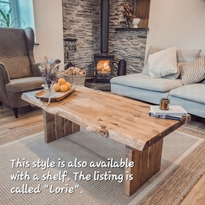 May include: A rustic wooden coffee table with a live edge design. The table has a natural wood finish and is supported by two chunky legs. The table is sitting on a rug in front of a fireplace.