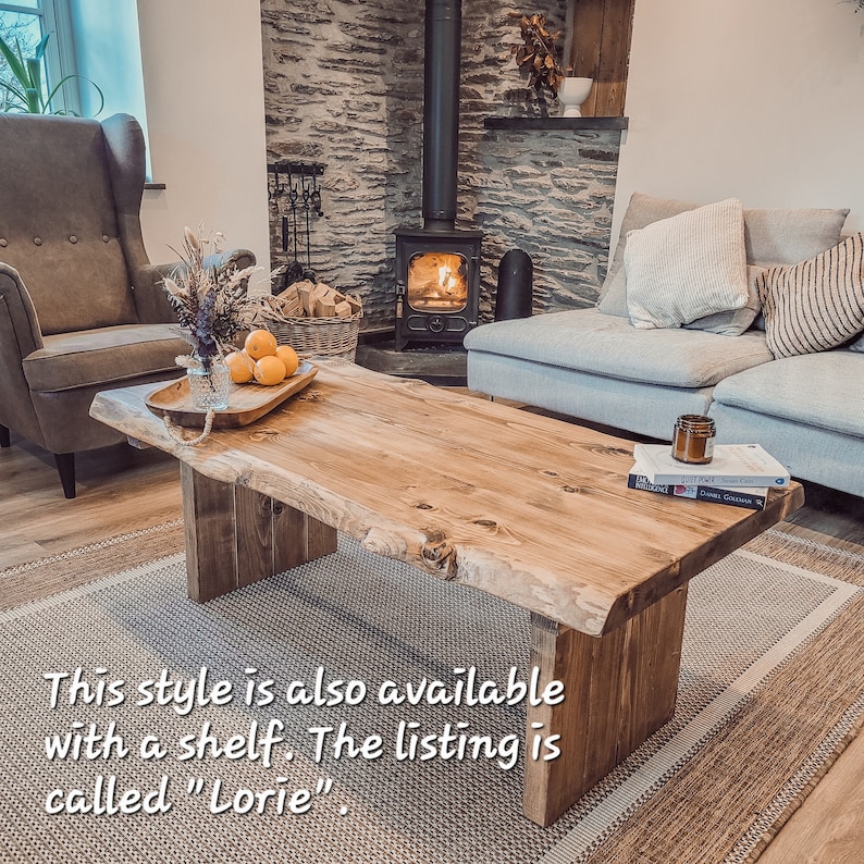 May include: A rustic wooden coffee table with a live edge design. The table has a natural wood finish and is supported by two chunky legs. The table is sitting on a rug in front of a fireplace.