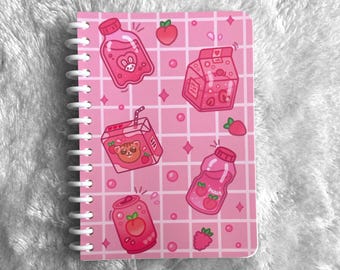 May include: Pink spiral-bound notebook with a repeating pattern of illustrated beverages and fruit. The design includes a bunny, a bear, and the word "Peach" on a bottle. The background is a grid pattern with pink diamonds and circles.