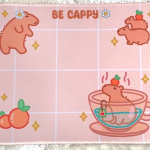 Könnte beinhalten: Ein rosa Mauspad mit einem Gittermuster und einem Cartoon-Capybara in einer Teetasse. Der Text "BE CAPPY" ist auf dem Mauspad gedruckt.